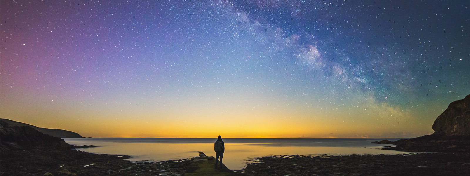 A man looking up at the starry sky at Port Soderick, on the east coast of the Isle of Man.