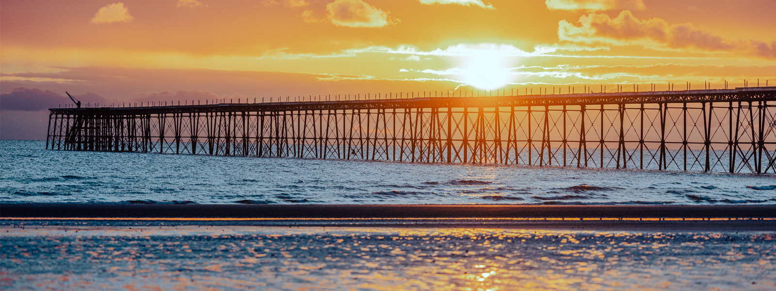 Queen's Pier on Ramsey Beach with the sun rising behind it