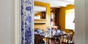 Bridge House Dalby – close-up of blue and white ceramic tile with pastoral scene, set in cozy dining room with traditional décor and yellow wall