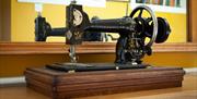Bridge House Dalby – vintage black sewing machine with floral design on wooden base, set against yellow wall with mirror, books