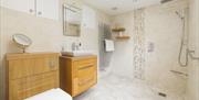 Bridge House Dalby – modern bathroom with wall-hung toilet, rainfall shower, mosaic tile detail, wooden vanity, towel radiator, and recessed lighting